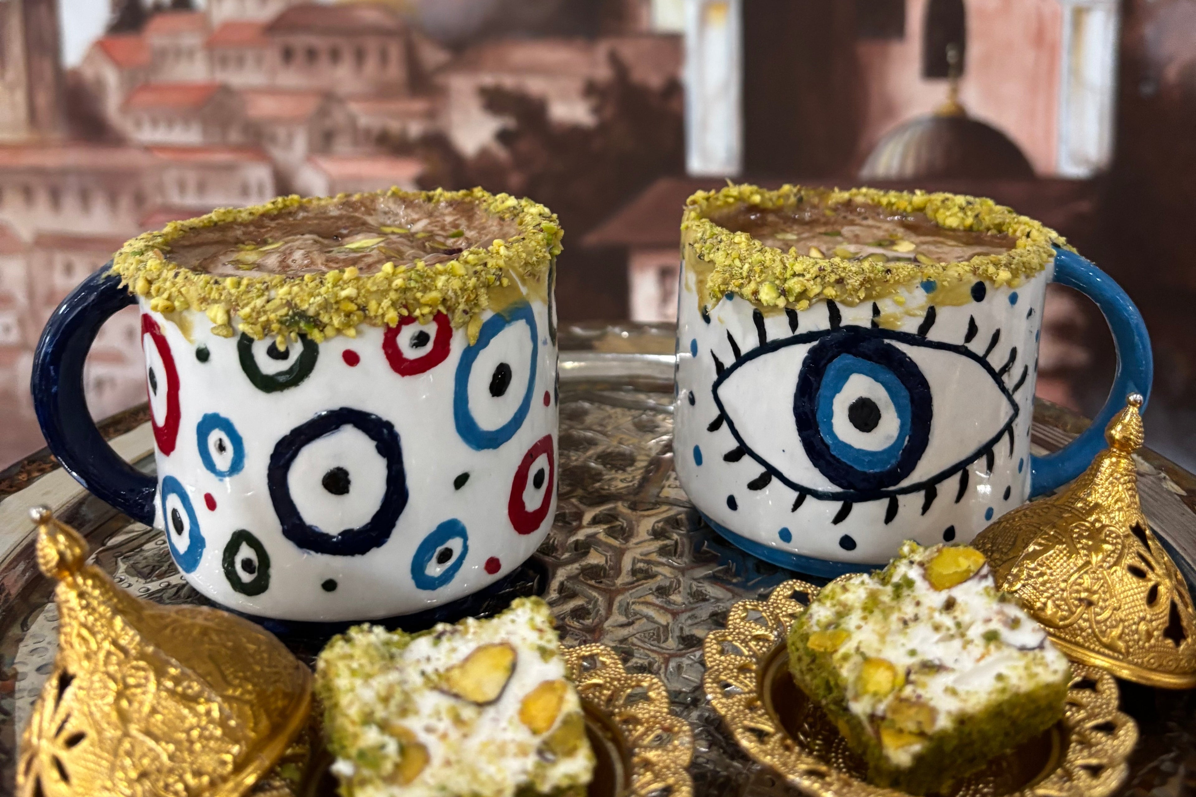 Decorative mugs with artistic designs on a surface with a blurred architectural background